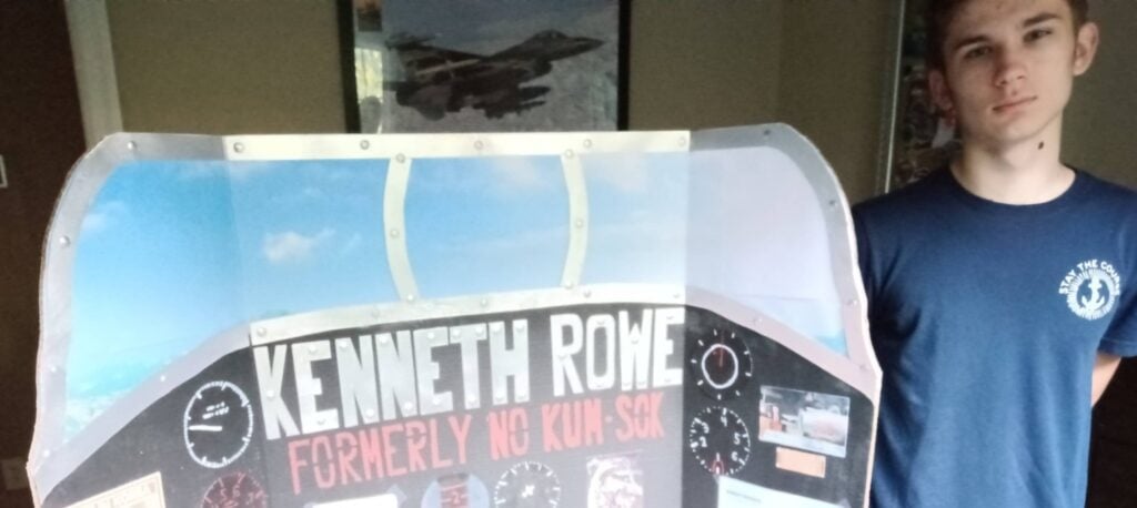 A teenage boy stands with a trifold poster that reads 'Kenneth Rowe.'