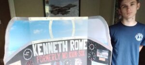 A teenage boy stands with a trifold poster that reads 'Kenneth Rowe.'